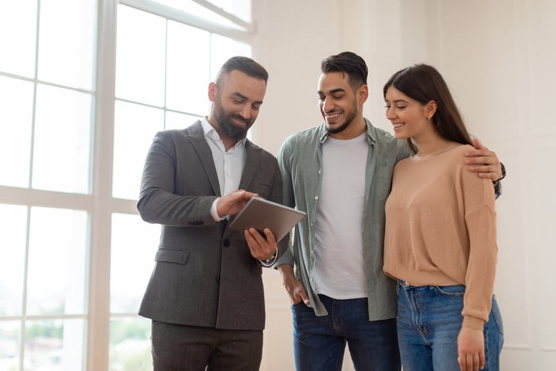 A South Asian couple reviews information on a tablet with a South Asian businessman
